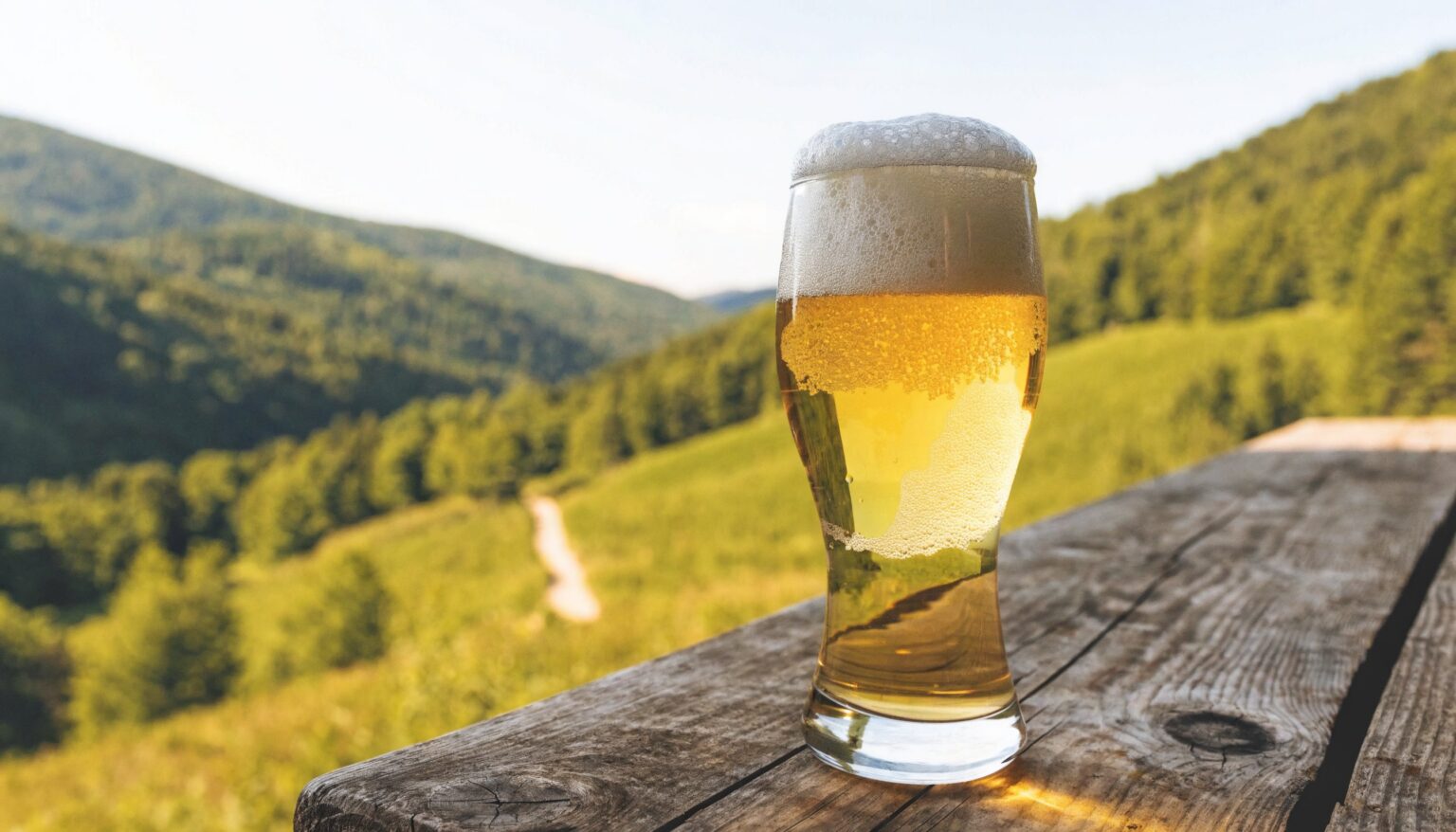 Glas regionales Bier auf rustikalem Holztisch mit Wanderweg in den Gaminger Hügeln