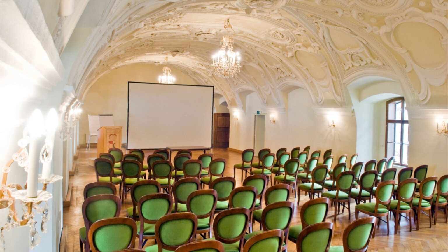 Barocker Seminarsaal mit Stuckdecke, Kronleuchtern und Bestuhlung mit Leinwand für Seminare und Teamtage in der Kartause Gaming