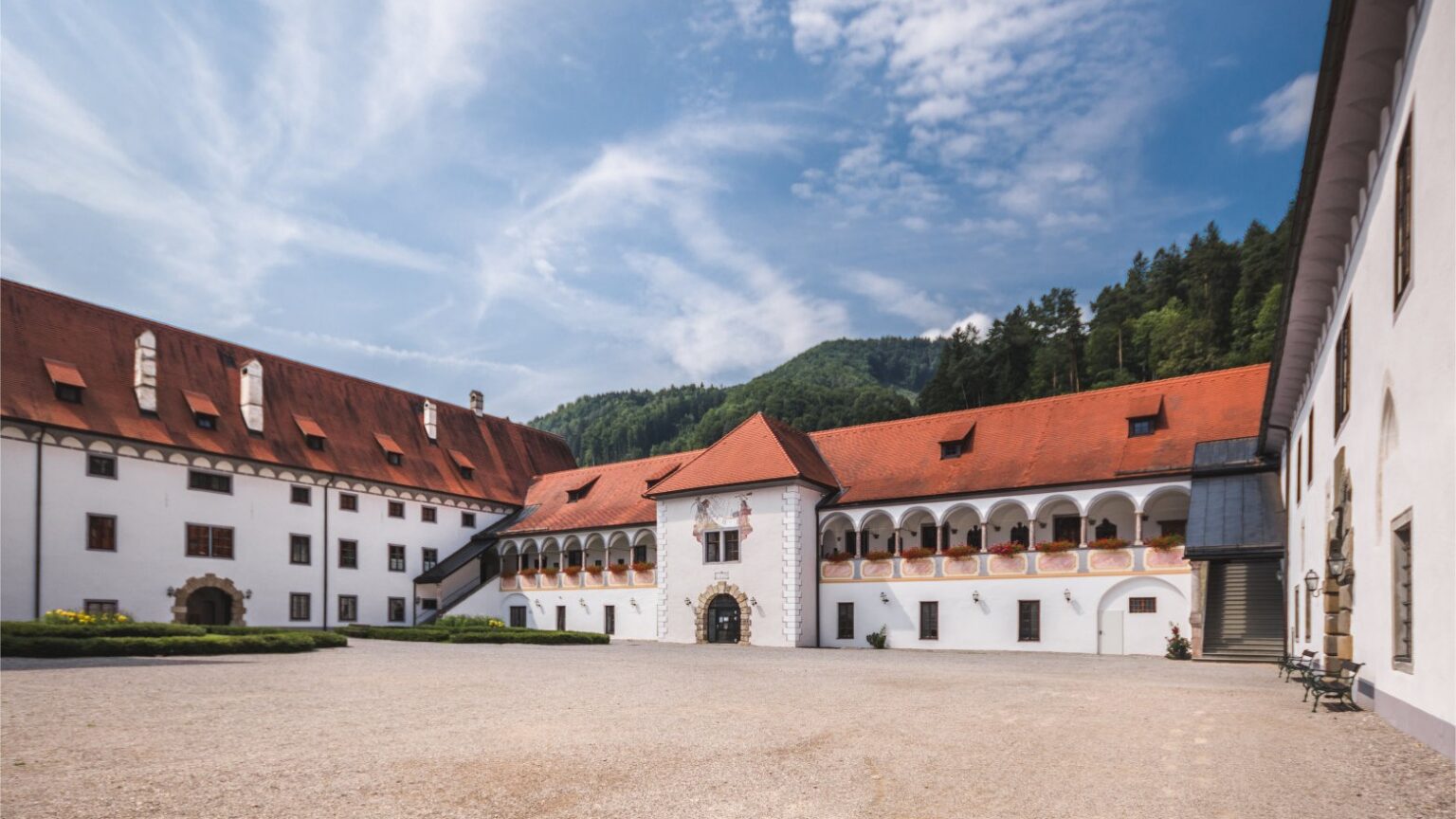 Prälatenhof der Kartause Gaming – ruhiger Klosterhof mit Arkaden, weiße Fassaden und rote Dächer vor bewaldeten Bergen