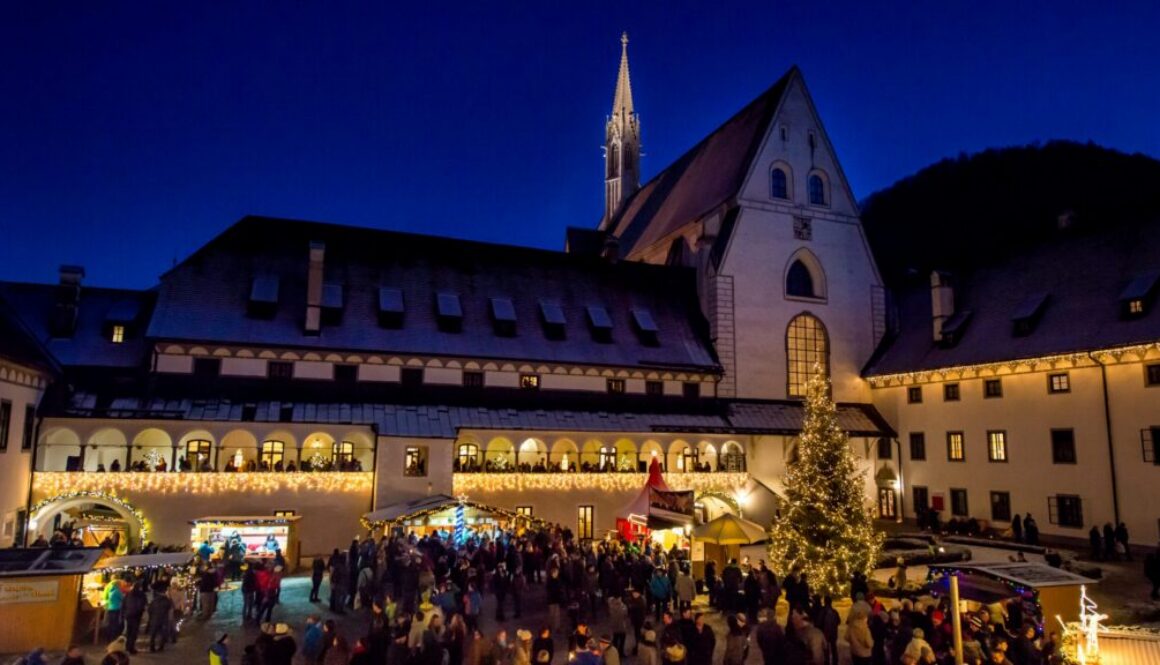 Adventmarkt im Mostviertel: beleuchtete Marktstände im Hof der Kartause Gaming mit Christbaum und Besuchern zur blauen Stunde