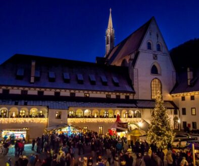 Adventmarkt im Mostviertel: beleuchtete Marktstände im Hof der Kartause Gaming mit Christbaum und Besuchern zur blauen Stunde